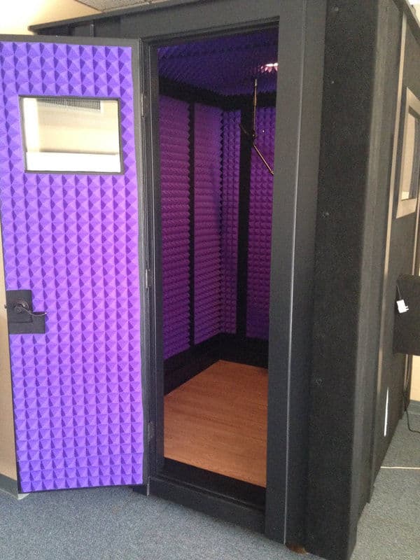 Soundproof vocal booth with purple acoustic panels and open door, ideal for recording.