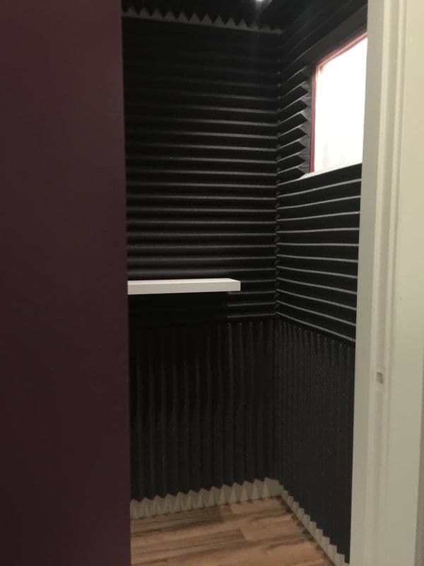Soundproof vocal booth with foam panels and a shelf, featuring a small window.