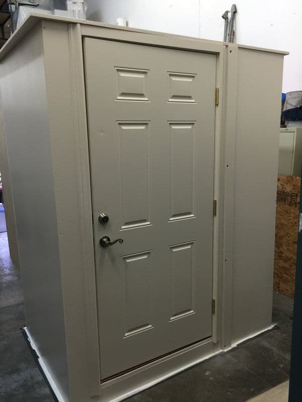 White, six-panel entry door with brass handle in a workshop setting.