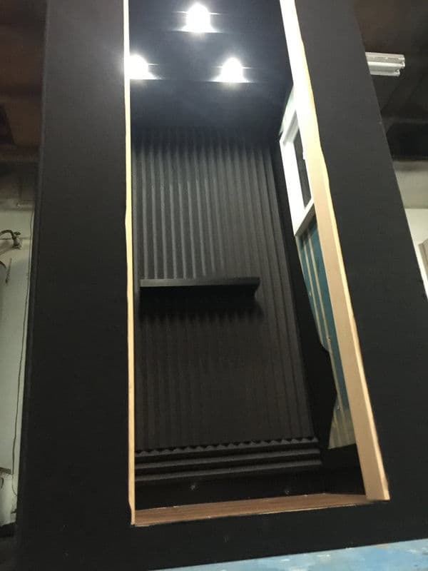 Interior of a black soundproof booth with recessed lighting and a shelf.