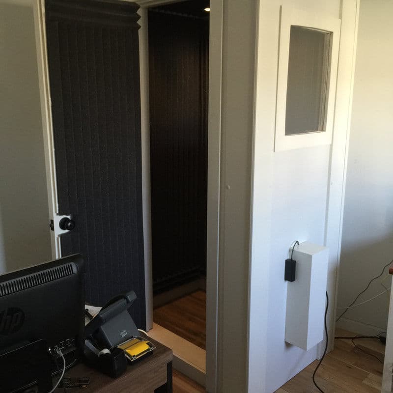Soundproof recording booth setup in an office with computer and phone on a desk.