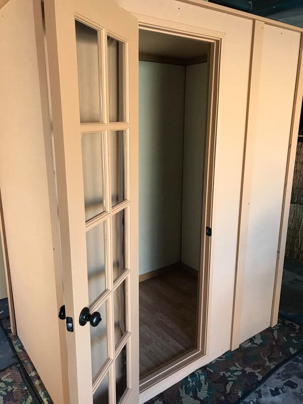 Interior view of a tan portable room with a glass door and wooden flooring.