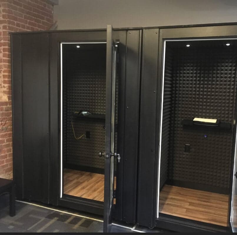 Soundproof recording booths with black walls and wooden flooring in a modern studio setting.
