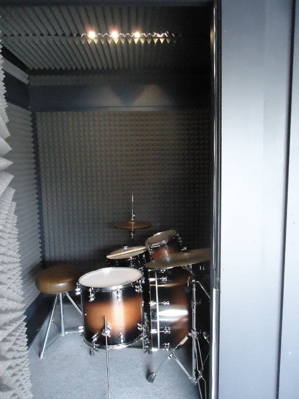 Drum set in a soundproof recording studio booth with acoustic panels.
