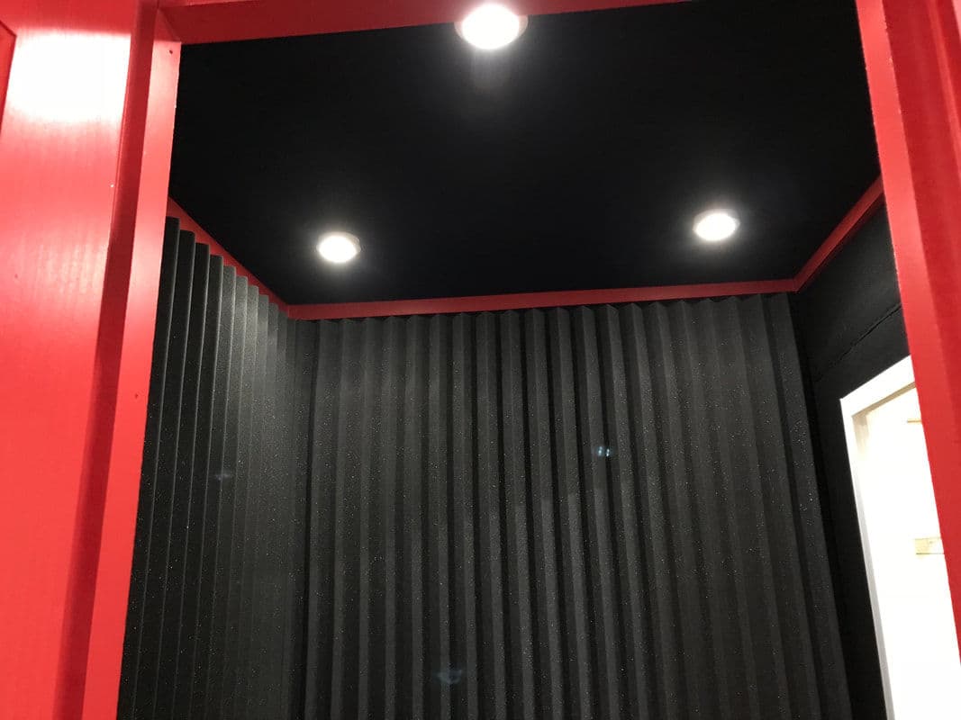 Interior of a soundproof room featuring black acoustic panels and red walls with ceiling lights.