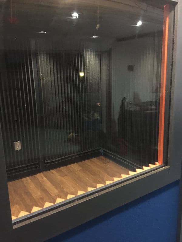 Soundproof recording studio booth with glass walls and wooden floor.
