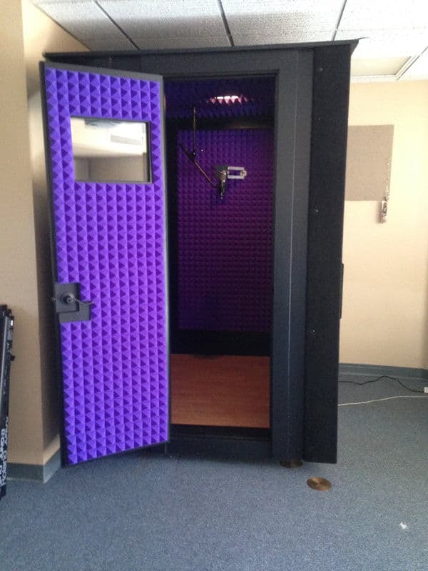 Soundproof recording booth with purple acoustic paneling and open door. Ideal for audio production.