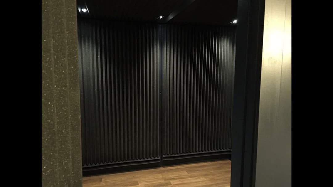 Interior view of a soundproof room with black ribbed walls and wooden flooring.