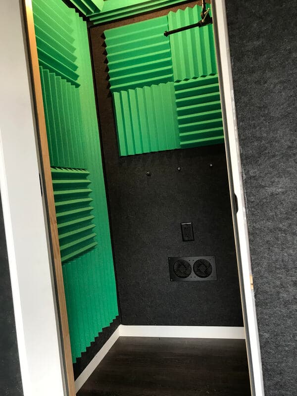 Soundproof recording booth with green acoustic panels and wall-mounted speakers.