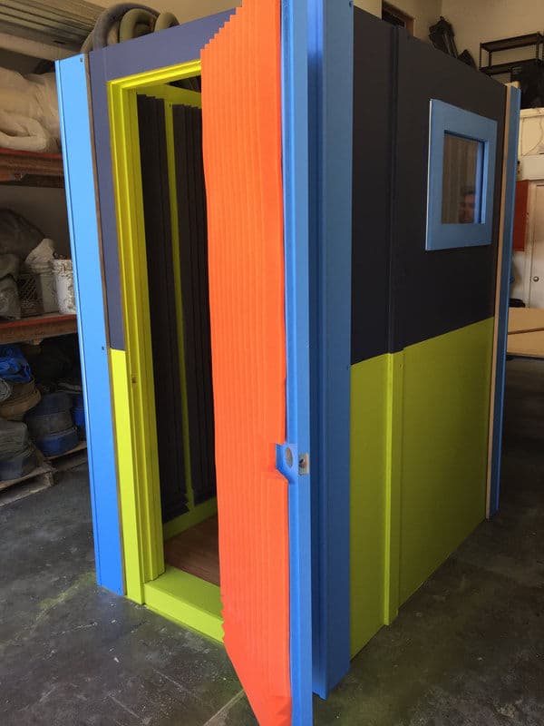 Colorful sound-proof booth with multiple panels, open door, and small window. Ideal for recording.