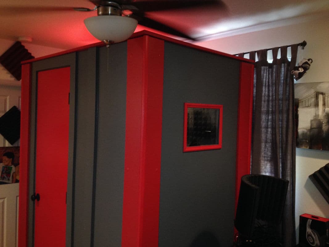 Soundproof recording booth with red and gray design, ceiling fan, and acoustic panels.
