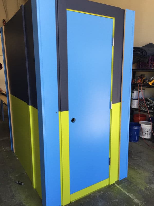 Colorful portable restroom unit with a blue and yellow design, set in a workshop environment.