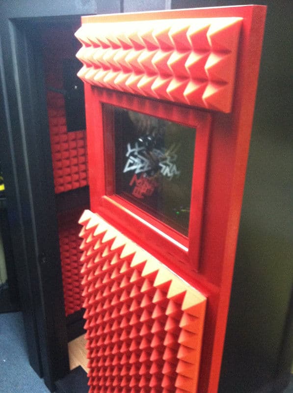 Red soundproof booth with textured acoustic panels and a window for studio recording.