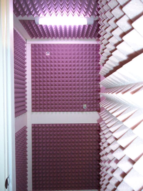 Soundproof recording booth with pink foam paneling for acoustic treatment.
