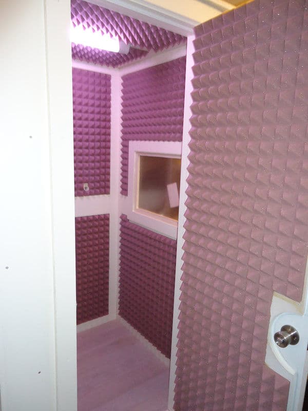 Soundproof recording booth with purple acoustic foam panels and a small viewing window.
