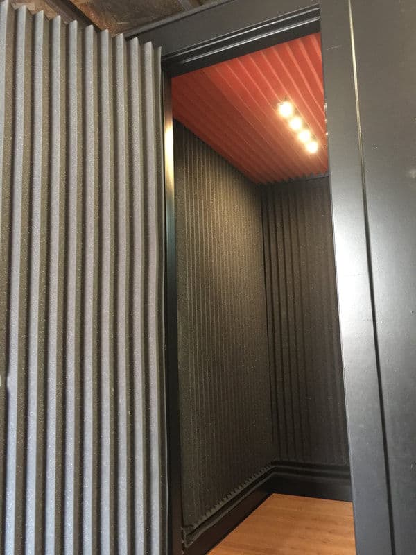 Soundproof recording booth with ribbed acoustic panels and warm ceiling lighting.