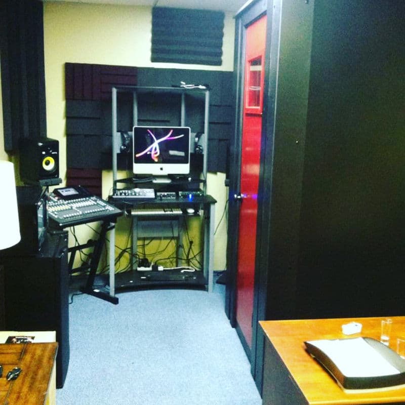 Recording studio with soundproofing, mixer, computer, and vocal booth for music production.