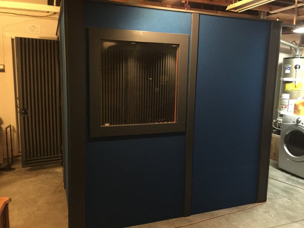 Soundproof recording booth with blue walls and a window, installed in a garage setting.