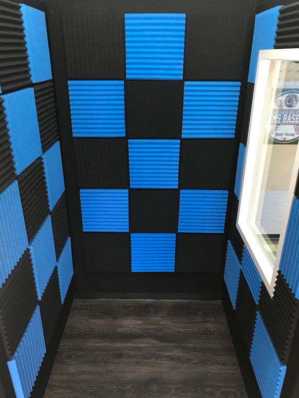 Acoustic treatment booth with blue and black foam panels and a window. Ideal for sound recording.