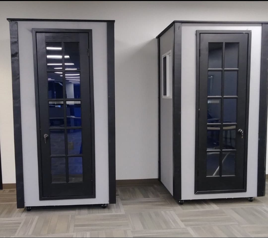 Two modern soundproof phone booths in an office setting with glass doors and windows.