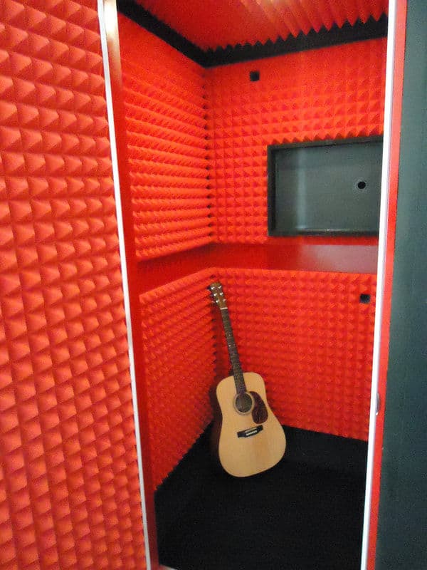 Acoustic soundproof room with red foam panels and an acoustic guitar resting inside.
