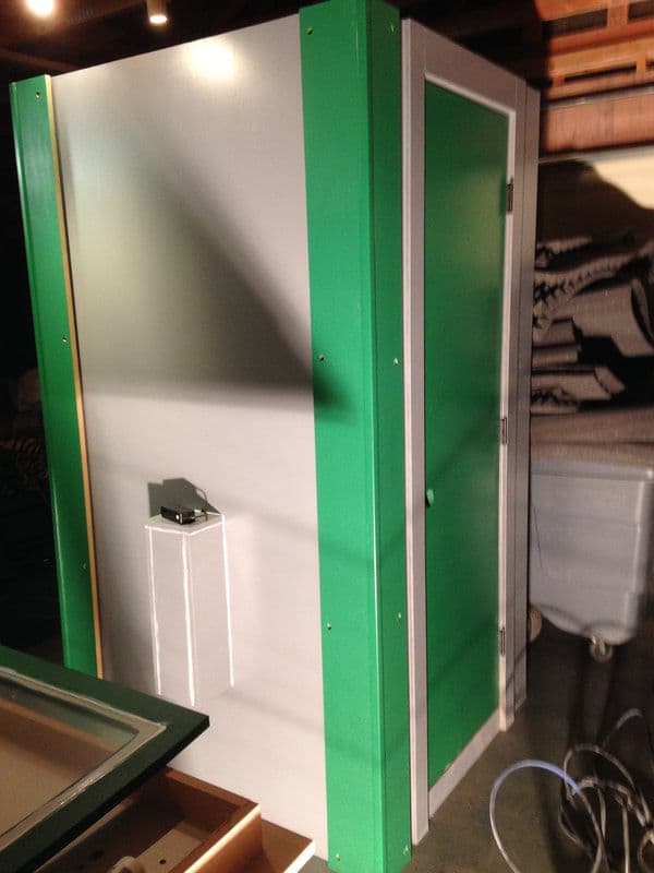 Compact green and white shower stall in a storage space with visible plumbing fixtures.