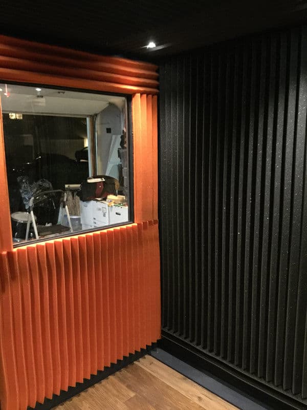 Soundproof recording studio with orange and black acoustic panels and a viewing window.