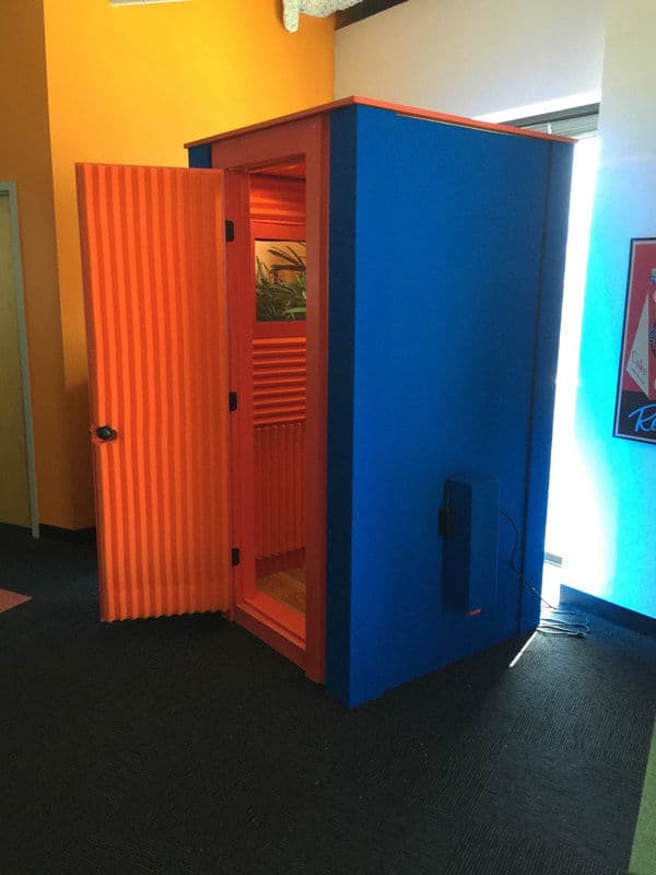 Vibrant blue and orange phone booth with an open door, set in a colorful interior space.