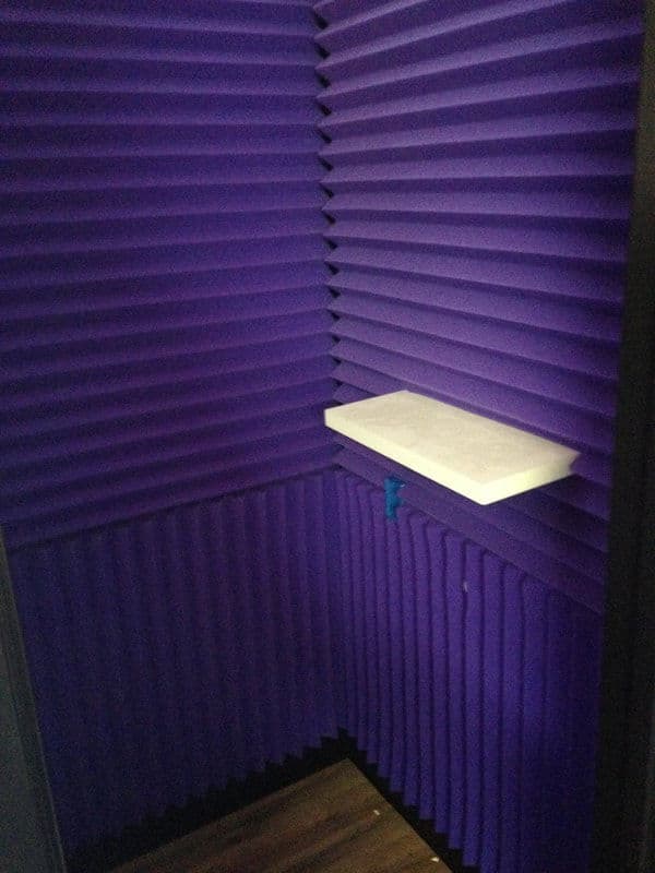 Soundproof recording booth with purple acoustic panels and a white shelf.