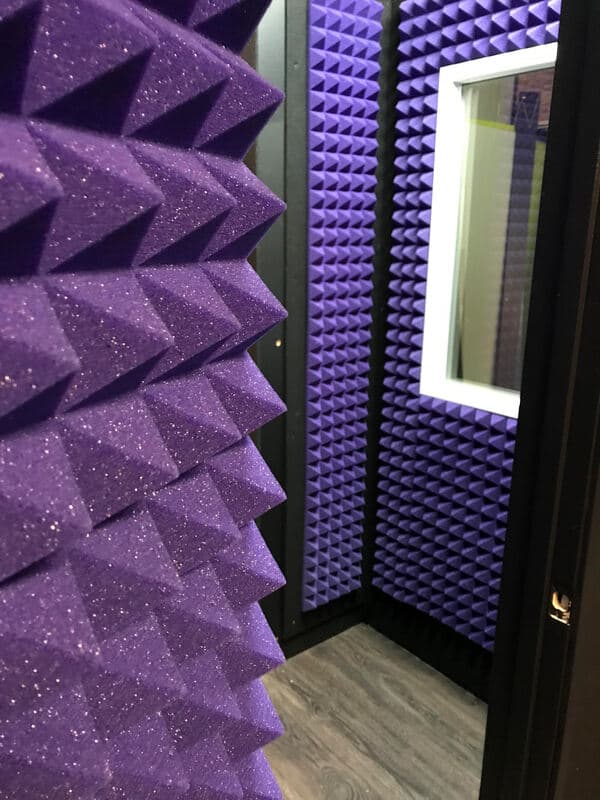 Acoustic soundproofing studio with purple foam panels and a viewing window.