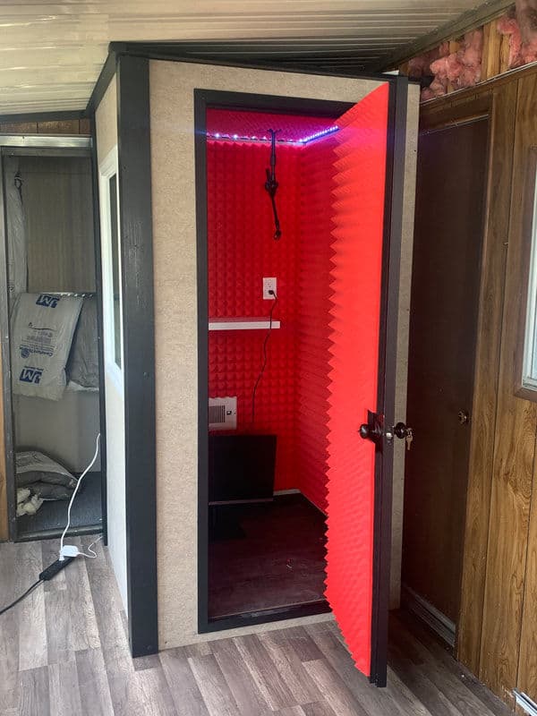 Vocal booth with red acoustic foam panels and a lighted interior for sound recording.
