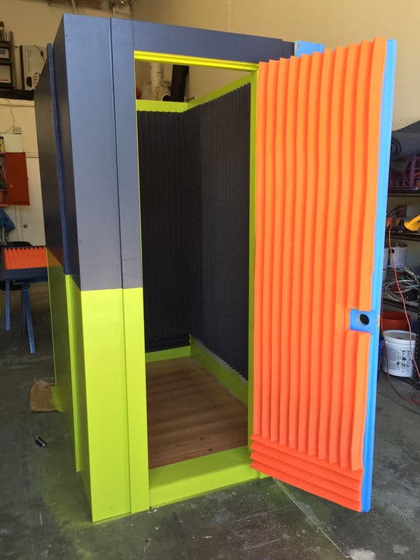Vibrant soundproof booth with orange and gray acoustic panels, wooden floor, open door.