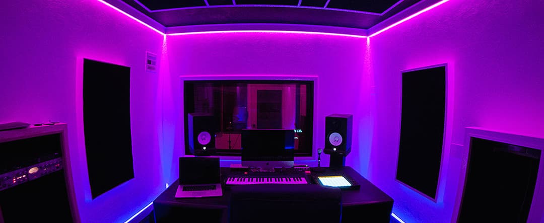 Modern music studio with purple LED lights, computer, keyboard, and speakers.