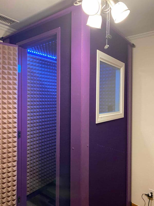 Vocal booth with purple soundproofing and LED lighting features, designed for recording.