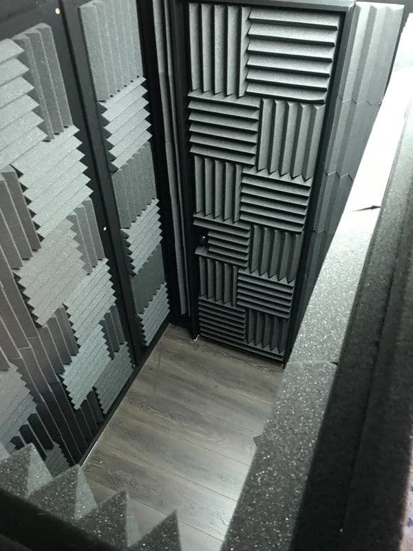 Acoustic treatment booth with foam panels and wooden flooring. Ideal for sound recording.