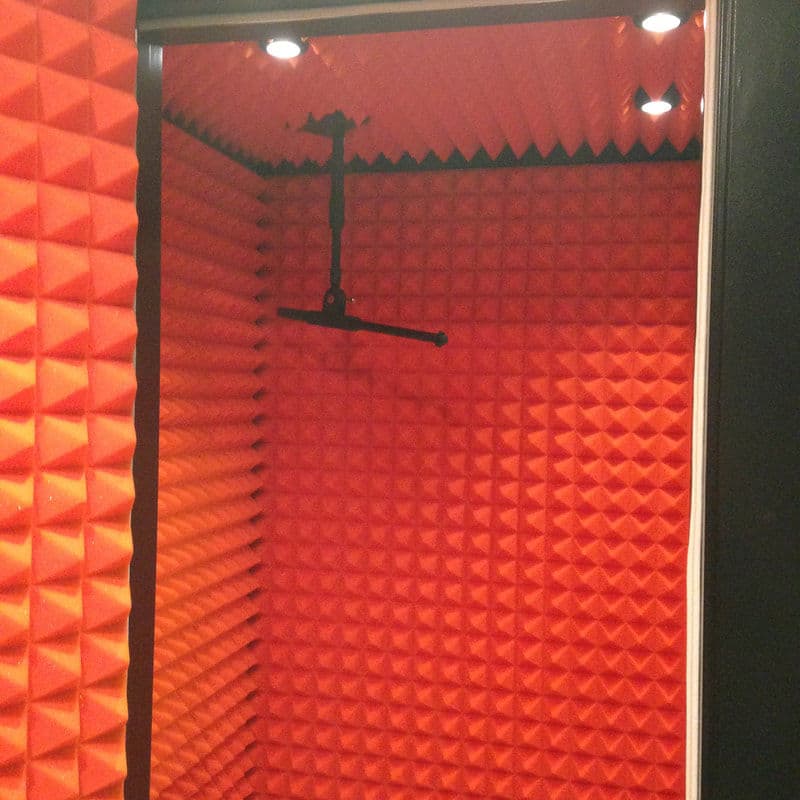 Soundproof recording booth with orange acoustic panels and microphone mount.