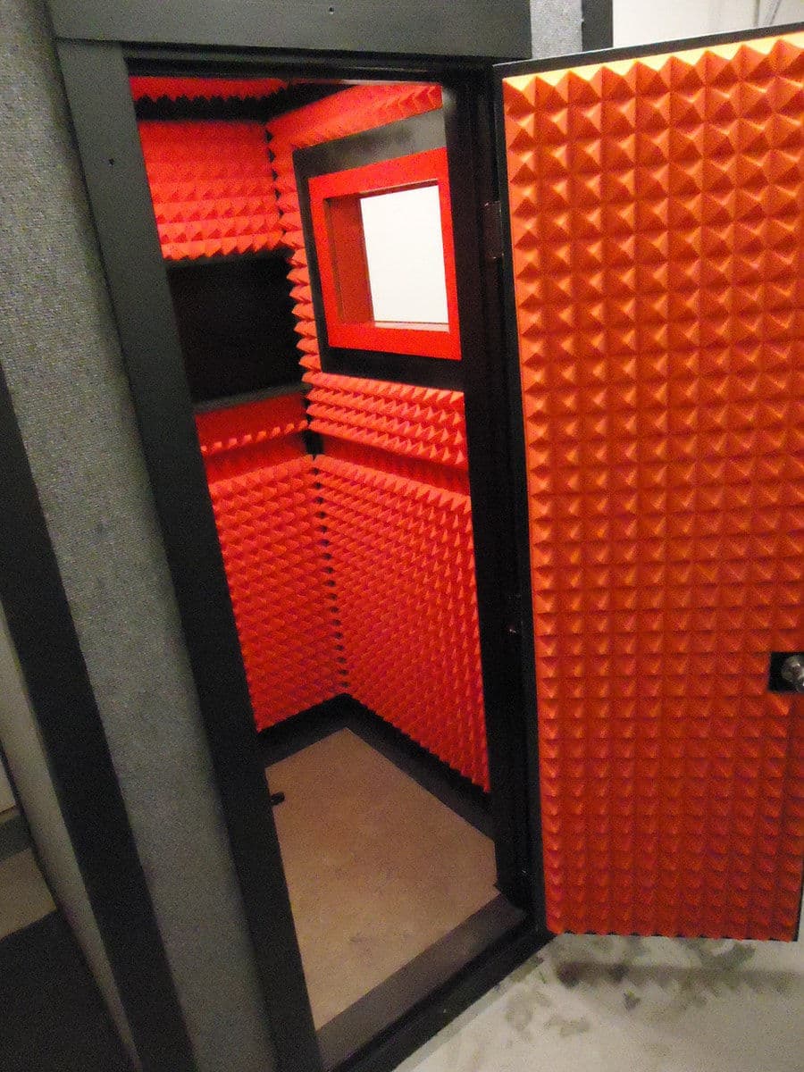 Soundproof recording booth with vibrant red acoustic foam interior and a glass observation window.