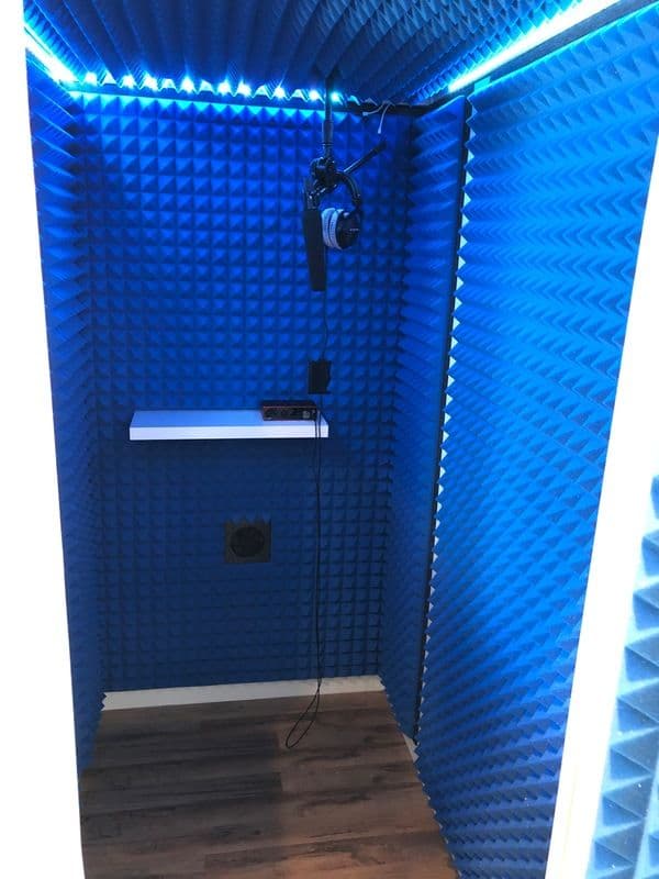 Blue soundproof recording booth with acoustic panels, microphone, and headphones.