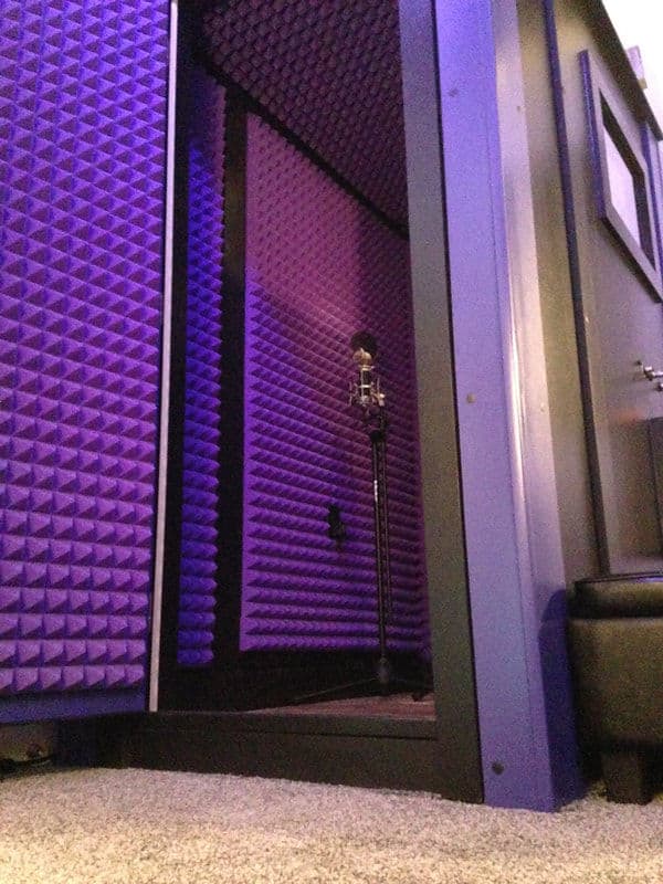 Vocal recording booth with purple acoustic foam and microphone stand.