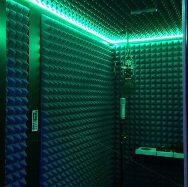 Acoustic soundproof recording studio with green LED lighting and microphone setup.