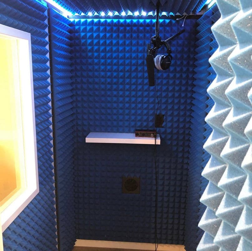 Soundproof recording booth with blue foam panels, microphone, and headphones for audio recording.