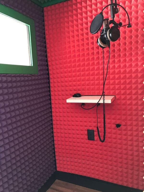 Colorful audio recording studio with red and purple soundproofing walls and hanging microphone.