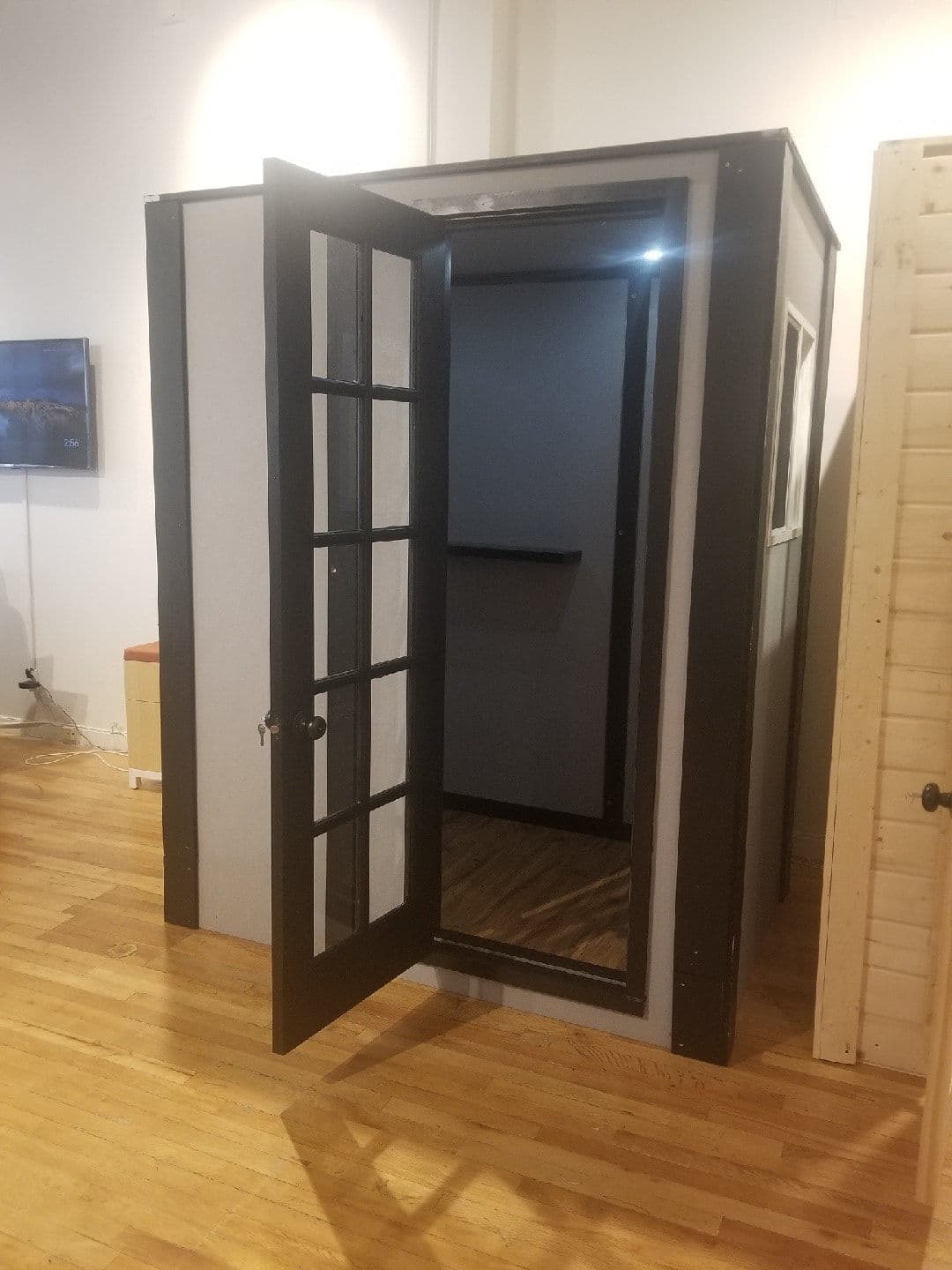 Open concept booth with black-framed door, showcasing interior and wooden flooring.