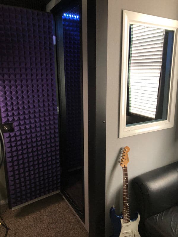 Vocal booth with soundproofing, window, and electric guitar in a recording studio setting.