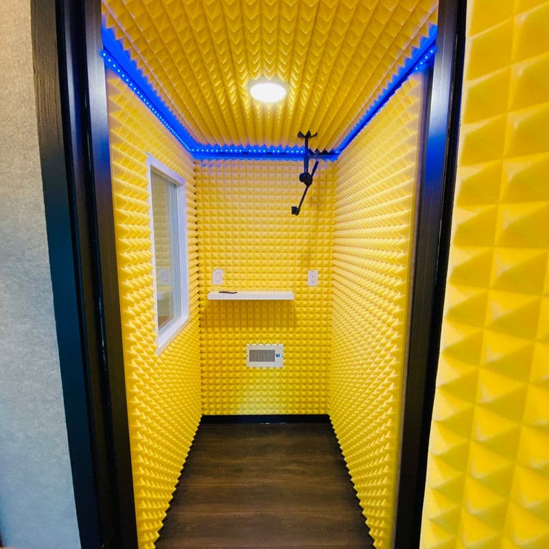 Vibrant yellow soundproof booth with acoustic panels and LED lighting for recording.