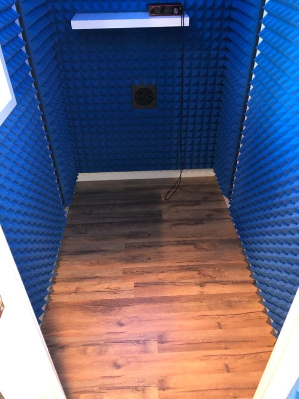 Soundproof recording booth with blue acoustic foam panels and wooden flooring.