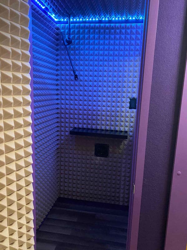 Soundproof recording booth with acoustic foam wall panels and blue LED lighting.