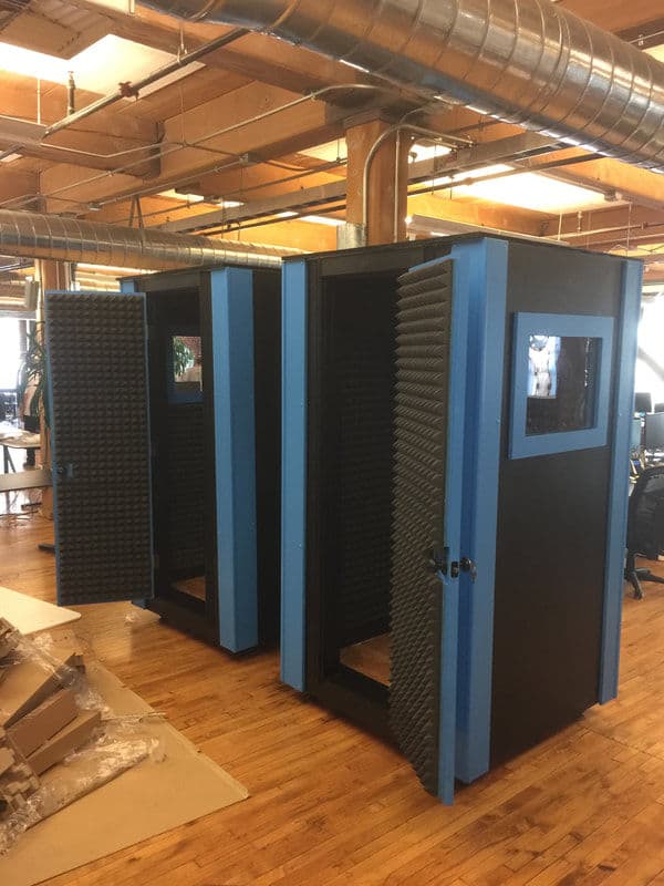 Two soundproof booths with open doors in a modern office setting, featuring acoustic panels.