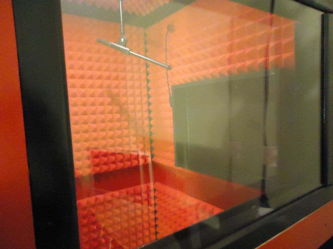 A soundproof recording studio with red acoustic panels and glass walls.