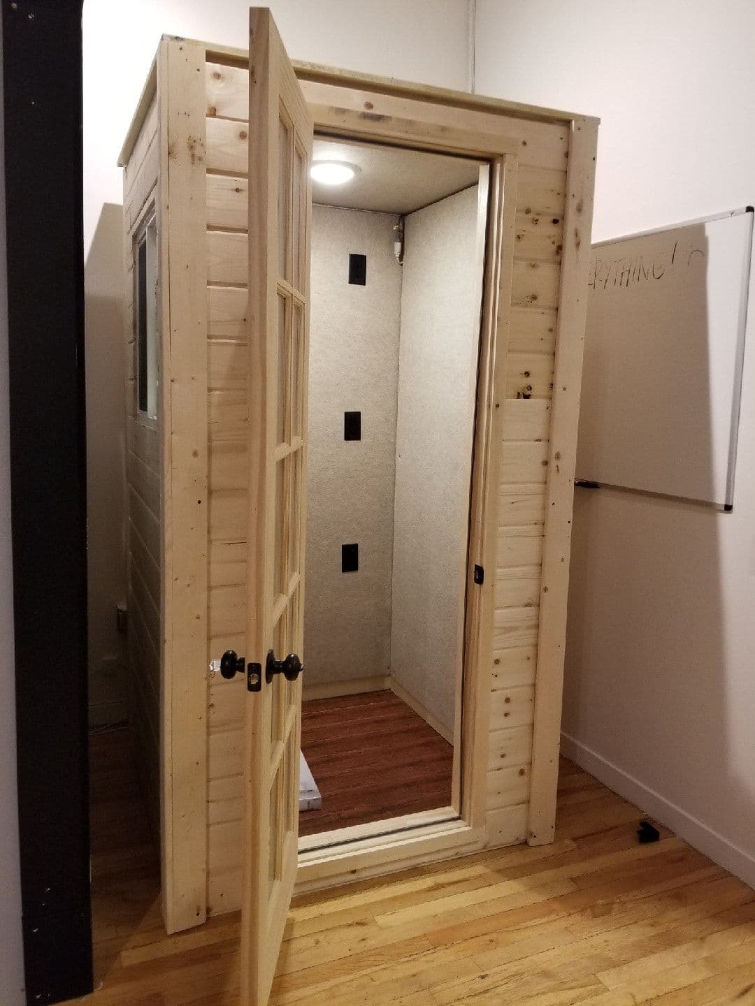 Wooden sauna booth with open door, minimalist design and interior lighting on hardwood floor.